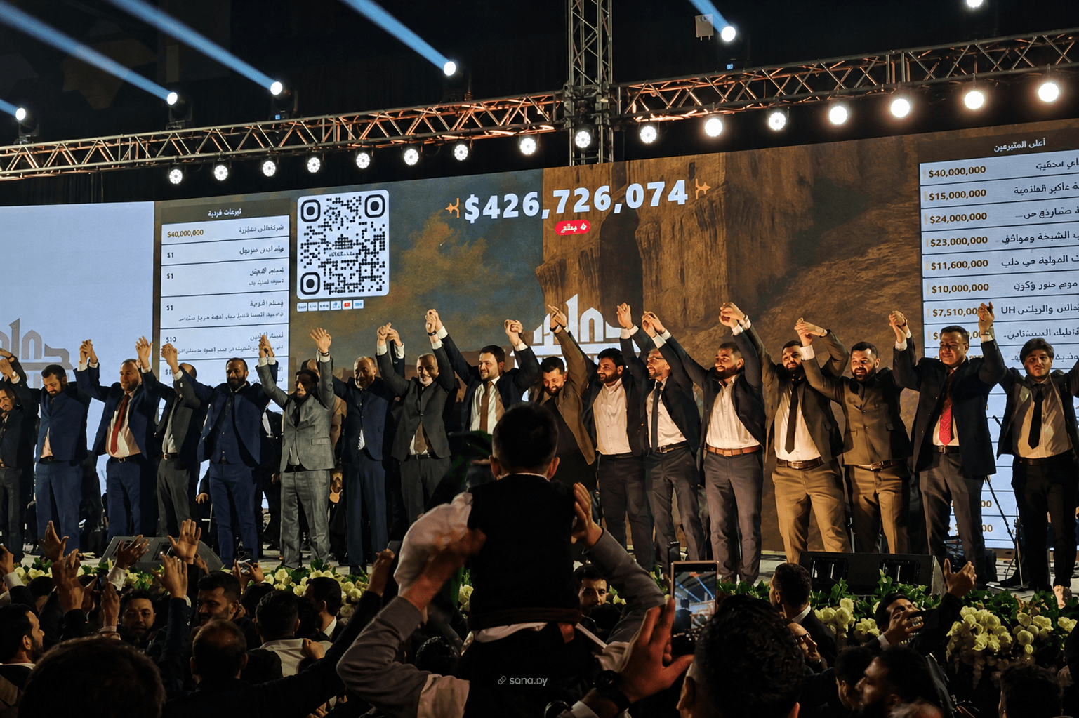 National fundraising event organizers holding hands on stage beneath the live donation total